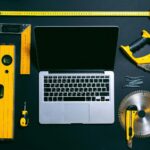 Overhead view of a laptop surrounded by various hand tools on a dark background, representing technology and construction.