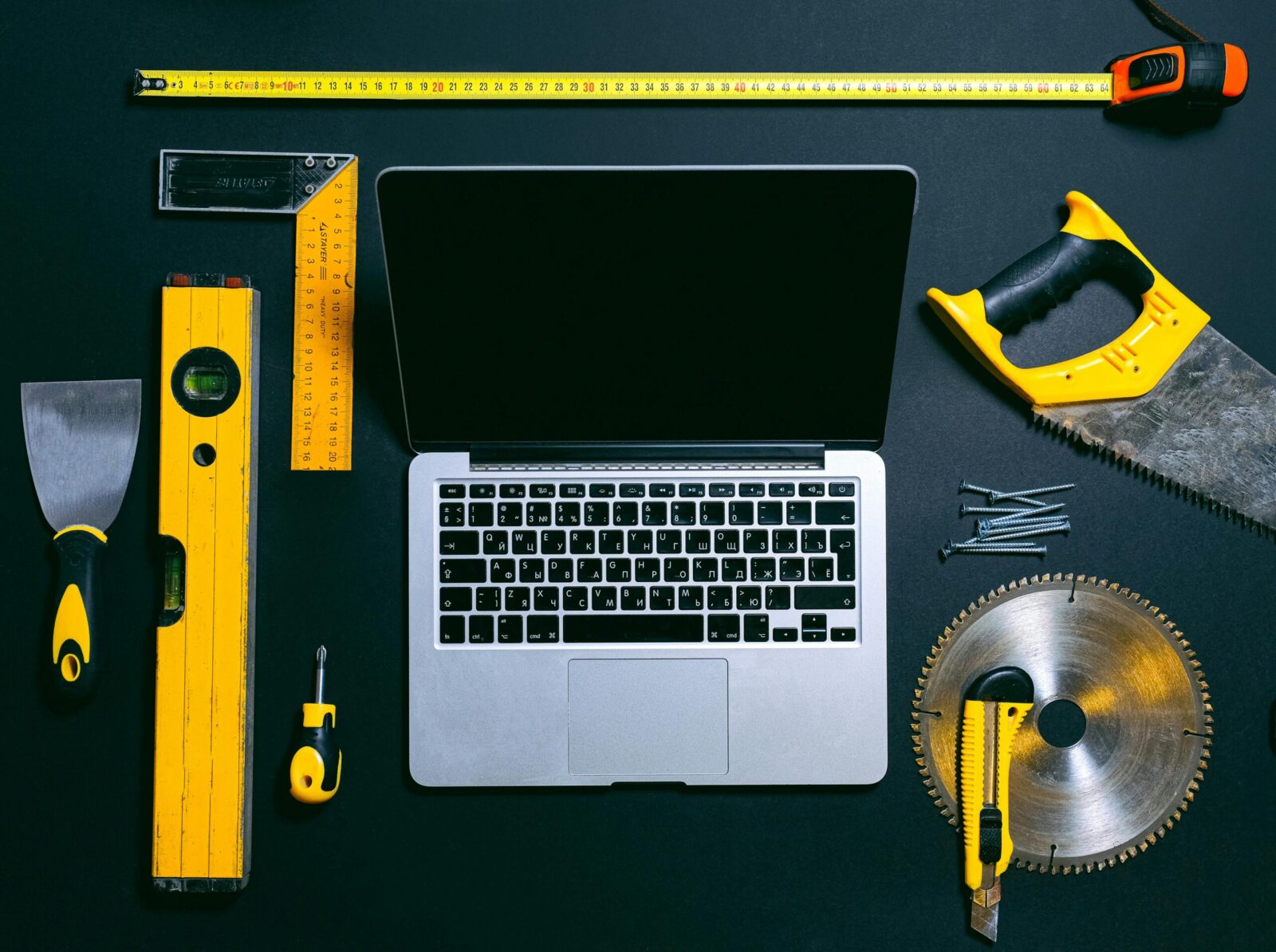 Overhead view of a laptop surrounded by various hand tools on a dark background, representing technology and construction.