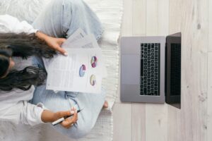 Top view of a woman studying charts on paper with a laptop, focusing on education and technology.