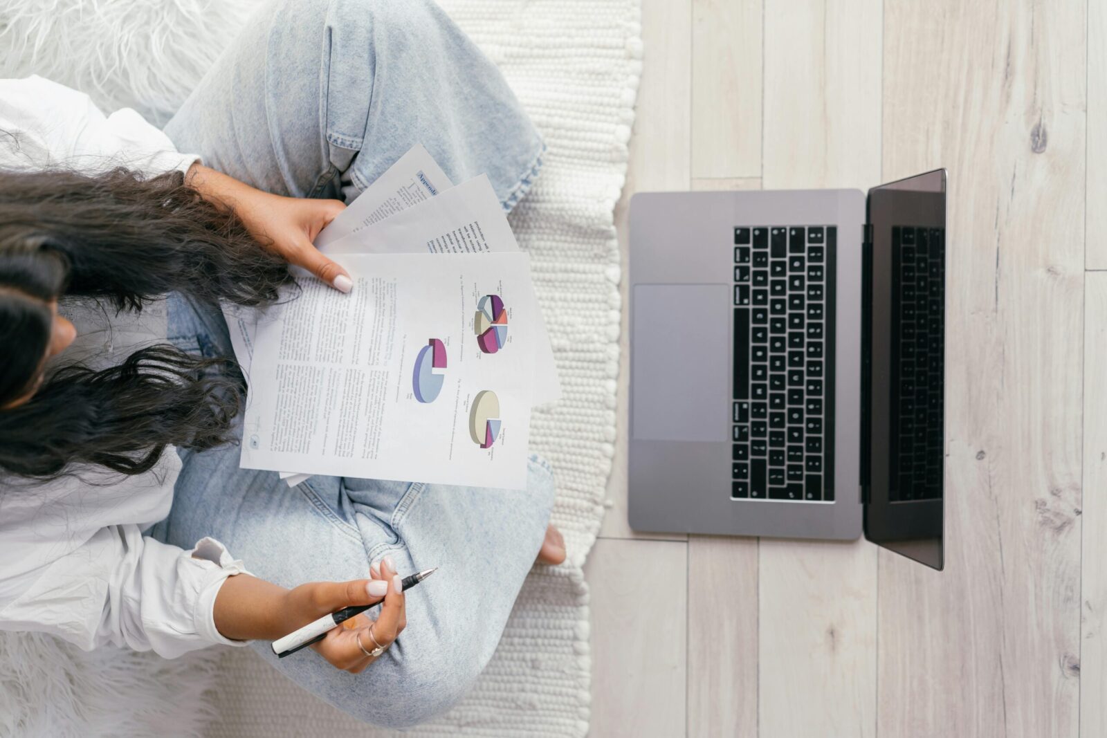 Top view of a woman studying charts on paper with a laptop, focusing on education and technology.